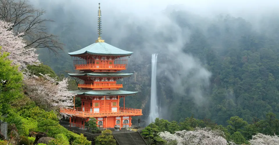 霧深い山に建つ朱色の五重塔と滝、桜並木